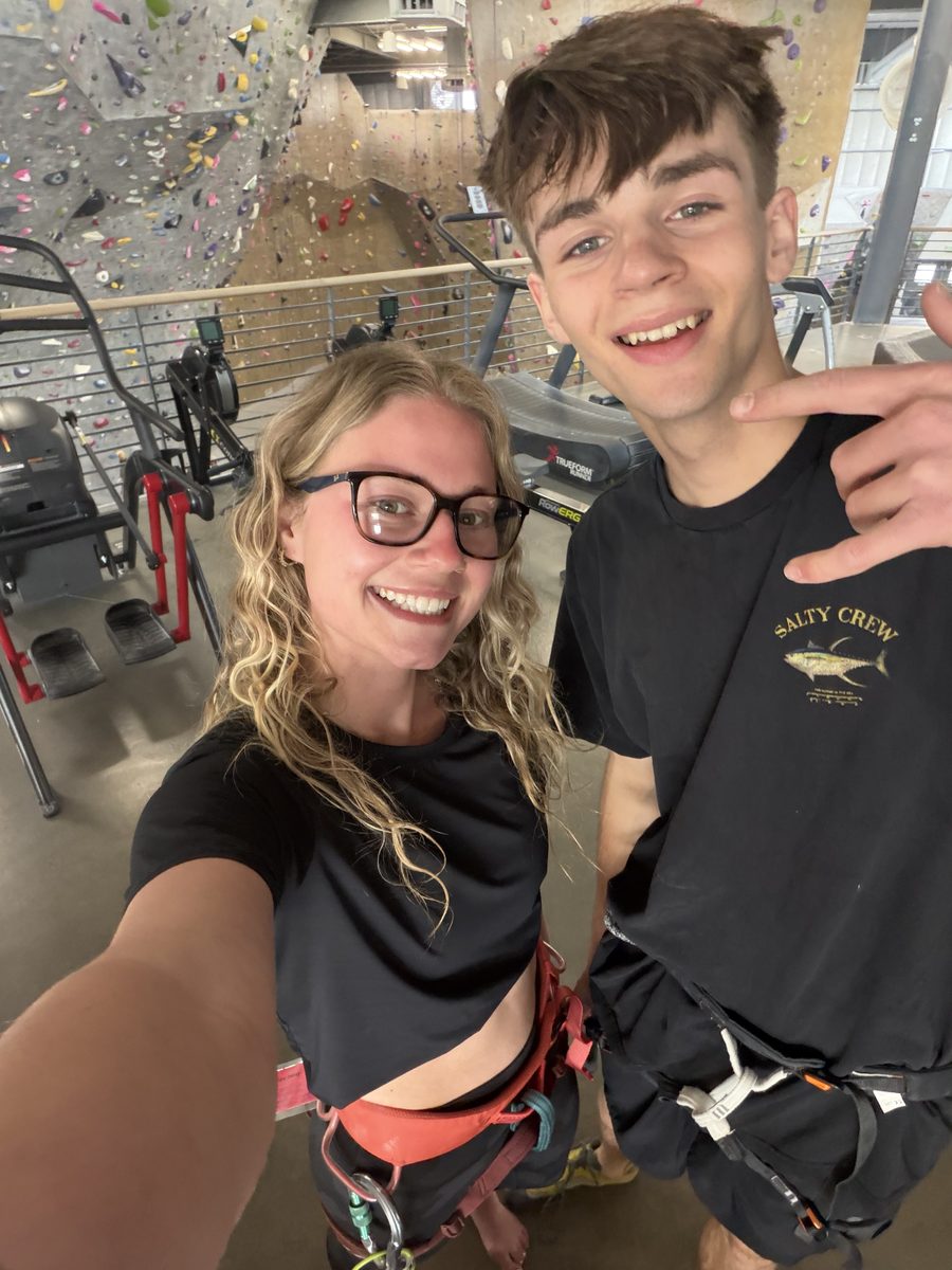 Gage and Grace in climbing harnesses at the climbing gym